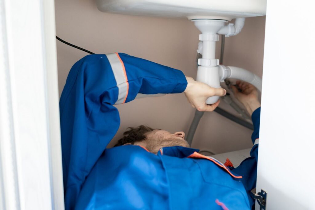 Plumbing answering service for plumbers: plumber repairing pipes under a kitchen sink